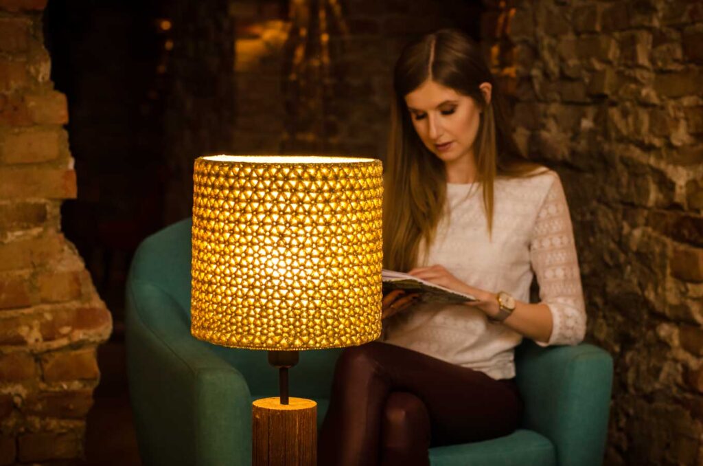 dziewczyna siedzi na fotelu, czyta książkę przy złotej lampie stołowej